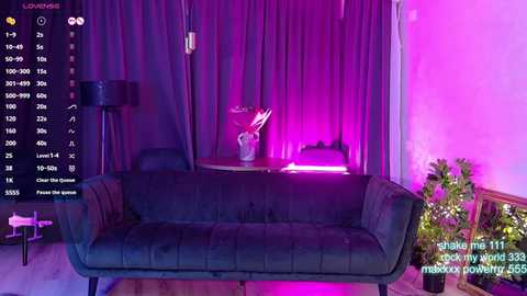Video of a modern, dimly lit living room with a purple-tinted ambiance. A dark green, tufted sofa sits against a purple curtain backdrop. A potted plant and a lamp are visible on the right.