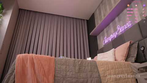 Media: Video of a modern bedroom with a plush, gray headboard, gray curtains, and a cozy, quilted bed in muted colors. Textured wall and soft lighting.