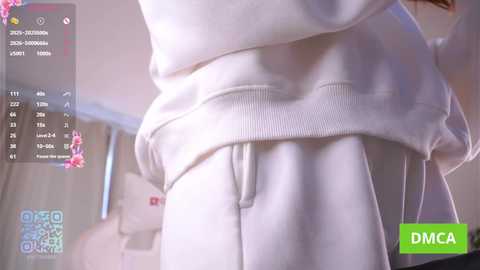Media: A video shows a person lifting their white sweatshirt, revealing their midsection. The background is blurred, featuring a window with light streaming in. The image includes a digital overlay with various numbers and text.