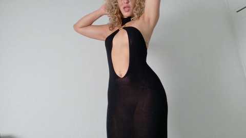 Video of a fair-skinned, curly-haired woman in a sheer black halter dress with a plunging neckline, posing against a plain white background.