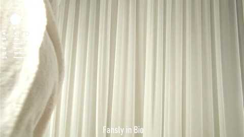Video of a close-up view of white pleated fabric curtains, with a soft, diffused sunlight creating a gentle, ethereal ambiance. The texture of the fabric is delicate and smooth.