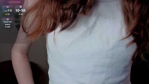 Media: Video of a woman's upper torso wearing a ribbed, sleeveless white tank top, with long, wavy brown hair. The background is dimly lit, and a digital display shows 10:50 time and temperature.
