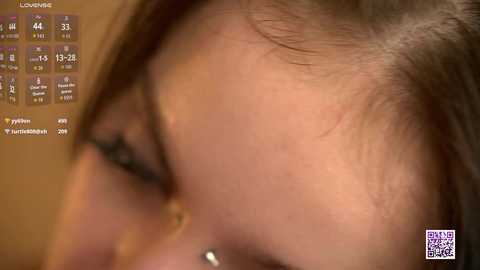 A close-up video of a young woman's face, with a mole on her cheek and light brown skin. The background features a blurred, warm-toned setting, and a \"Loveliv\" logo with a calendar is visible.