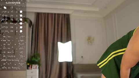 Video of a modern, well-lit room with a green shirt-wearing person in the foreground, beige curtains, and a bright white light source.