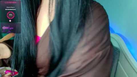 Video of a close-up of a woman with long, straight, black hair and fair skin, wearing a dark brown top, sitting indoors near a blue-lit wall.