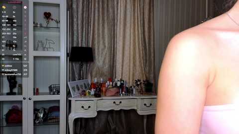 Video of a woman\u2019s bare back in a luxurious, dimly-lit room with a vanity table adorned with cosmetics and a black lamp.