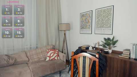 Media: Video of a cozy living room with beige sofa, floral throw pillows, wooden desk, two framed botanical prints, tall lamp, and a striped chair.