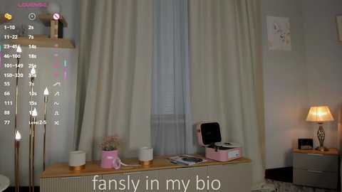 Video of a cozy, pastel-colored bedroom with a wooden desk, potted plants, a pink record player, and a lamp, featuring a text overlay: \"fansly in my bio.\