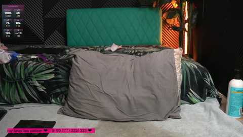 Video of a messy bedroom with a green quilt, a gray pillow, a pink phone, and a water bottle on a carpeted floor.