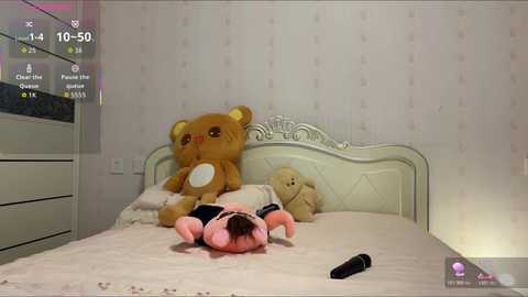 Video of a plush bear and a pink plush toy on a bed, with a digital clock displaying 10:04 and a smartphone screen visible in the bottom right.