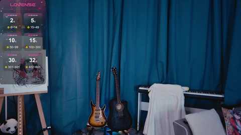 Video of a cozy music room with a teal curtain backdrop. A guitar and bass guitar stand on a wooden table, next to a white cloth. A music stand displays song lyrics and chords, and a digital metronome is visible.