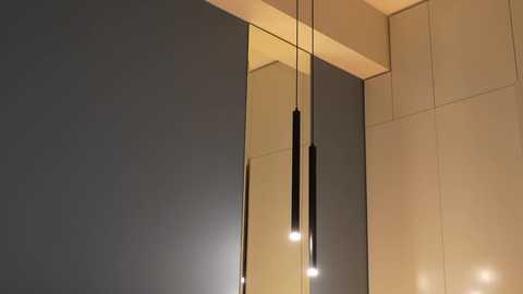 Video of a modern, minimalist room with dark gray and beige paneled walls. Two black, slender pendant lights hang from the ceiling, casting a warm, soft glow.