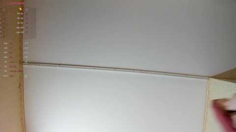 A video showing a person with a pink shirt and a dark object partially obscuring a whiteboard calendar with a date in the top left corner. The background is plain beige.