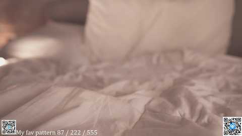 Media: Video of a cozy, rumpled beige bedspread with a blurred background, featuring a watermark and QR code in the bottom left corner.