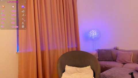 Video of a cozy living room with a gray armchair, beige cushions, orange curtains, and a purple LED light in the background, capturing a serene, warm ambiance.