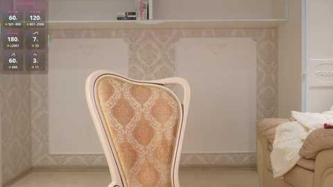 A video of a beige, patterned upholstered chair in a room with cream-colored walls and a white, ornate wooden cabinet. The room has a warm, elegant ambiance.