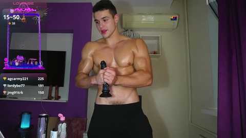 Media: Video of a shirtless, muscular young man with short dark hair, holding a black dildo in a dimly lit room with purple walls.
