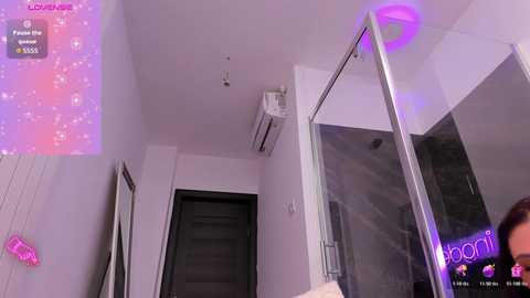A video of a modern, minimalist bedroom with white walls, a glass shower, and a neon \"doori\" sign.