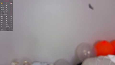 A blurred video of a bedroom with a white wall, an orange pillow, and a black silhouette of a person or object in the upper left corner.