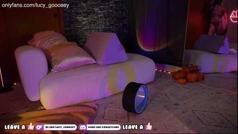 A video shows a white, plush sofa with a black circular object in the foreground, surrounded by Halloween-themed decor, including pumpkins and a stone wall background.