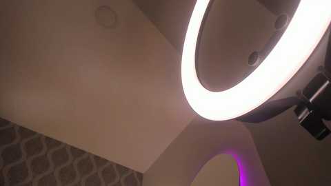 A video of a modern ceiling with a circular, glowing white light fixture and a textured, patterned wall in neutral tones.