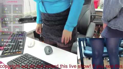 A video shows a woman in a blue top and black skirt, adjusting her skirt, seated at a desk with a computer keyboard and mouse.