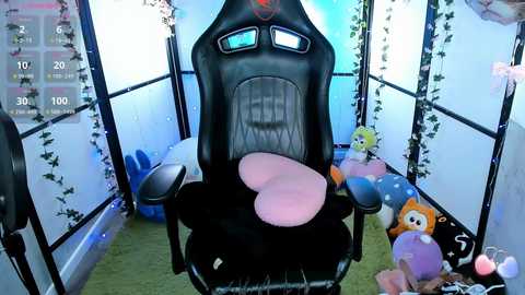 Video of a plush, black gaming chair with pink cushions, surrounded by plush toys and fairy lights, in a cozy, pastel-colored room.