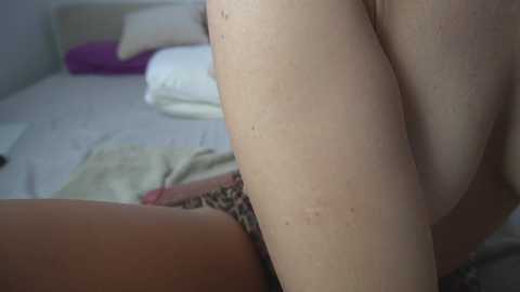 Media: Video of a nude woman with fair skin, lying on a bed with leopard-print underwear visible. The background features a white bed with pillows and a purple pillow.