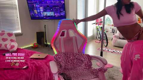 Video of a young woman in a pink, leopard-print outfit, adjusting a gaming chair in a colorful, themed bedroom with a TV and gaming setup.