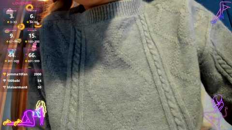 Video of a person wearing a grey, textured, cable-knit sweater with a high collar. Background features digital overlays, including a chat window with user names, timestamps, and emojis.