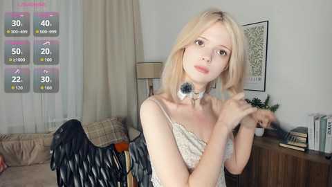 Media: Video of a young, fair-skinned, blonde woman with a slender physique, wearing a white, sleeveless dress, in a cozy, beige-themed living room with a lamp, books, and a framed picture.