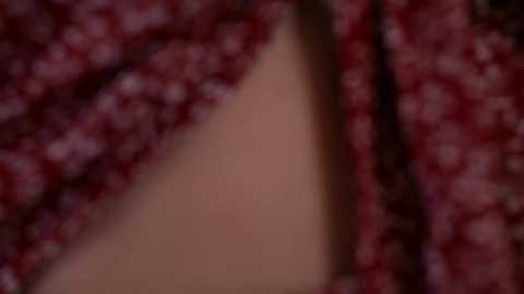 A blurred close-up video of a person with light skin, wearing a red floral-patterned shirt. The image is out of focus, making it difficult to discern details.
