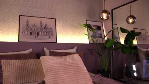 Media: Video of a modern bedroom with a beige headboard, two potted plants, a striped pillow, and framed architectural art on a patterned wallpaper.