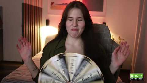Video of a woman with long dark hair, closed eyes, and a serene expression, sitting on a gray couch. She holds a large, colorful pinwheel. A warm, dimly lit room with a modern decor is visible in the background.