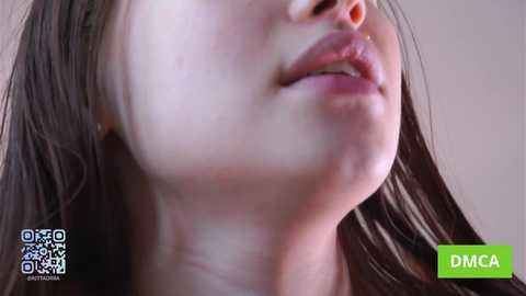 Video of a close-up of a young woman with light skin, dark hair, and a faint bruise on her cheek. Background is blurred.