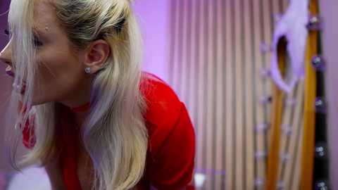 Media: A video of a blonde woman with long hair, wearing a red top, bending over with her mouth open, captured in a blurred, lively indoor setting.