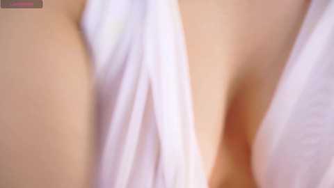 A close-up video of a woman's bare chest, with her left breast partially exposed, covered by a white towel. The skin is fair, and the towel has a soft, smooth texture. The background is blurred.