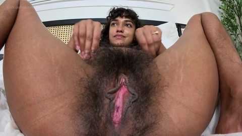 Media: Video of a nude woman with curly hair, light skin, and dark pubic hair, spreading her legs to reveal her vagina, taken from a low angle.