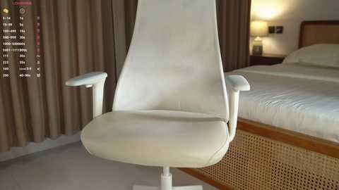 Video of a modern, white leather recliner chair with armrests in a minimalist bedroom with a wooden bed and beige curtains.