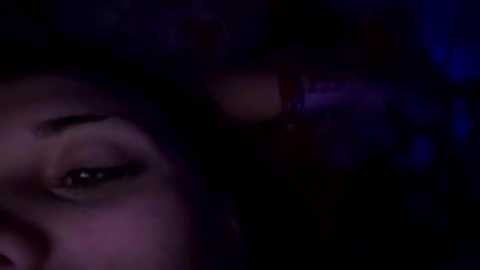 A dimly lit, grainy video captures a close-up of a person's face with dark, heavy eyelids, hinting at sleep or deep thought. The background is blurred, adding a mysterious, intimate atmosphere.