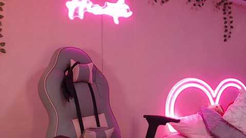 Video of a cozy room with a pastel blue gaming chair, pink neon heart light, and green foliage wall decor, creating a vibrant, playful atmosphere.