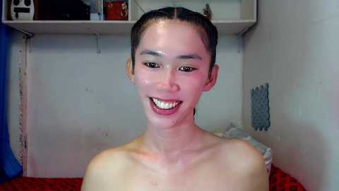 Video of a smiling, fair-skinned Asian woman with long black hair pulled back, wearing a white top, standing indoors against a white wall with shelves and a blue curtain.