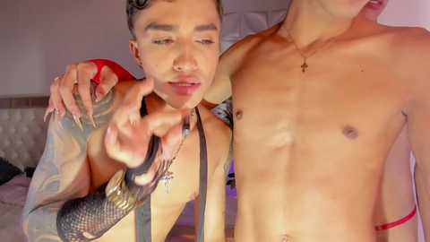 Video of a shirtless, tattooed, light-skinned Asian man holding a snake, with another shirtless man in the background, both in a dimly lit room.