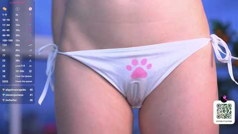 A video of a person wearing a white bikini bottom with a pink paw print design, taken from a low angle, with a blurred background and social media app interface visible on the left side.