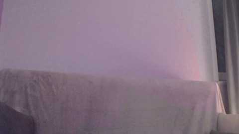 A video captures a white bedsheet draped over a gray surface, possibly a couch or table, with a soft, diffused light creating a pastel hue. The scene is minimalist and neutral, evoking a calm, serene atmosphere.