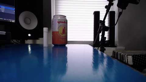 Video of a cluttered desk with a blue surface, a can of pineapple juice, a white cup, a speaker, and a microphone.
