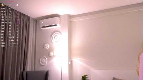 Video of a modern, minimalist room with white walls, grey curtains, a white AC unit, and a sleek lamp; a digital clock displays time and weather.