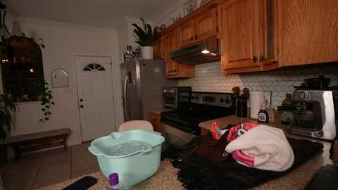 Video of a cozy kitchen with wooden cabinets, stainless steel appliances, white subway tiles, and a turquoise plastic tub filled with water on the counter.