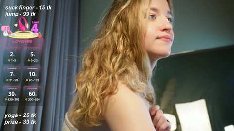 A video of a smiling young woman with long, wavy blonde hair, wearing a sleeveless top, standing indoors against a dark green wall. A digital fitness app overlay displays her stats.