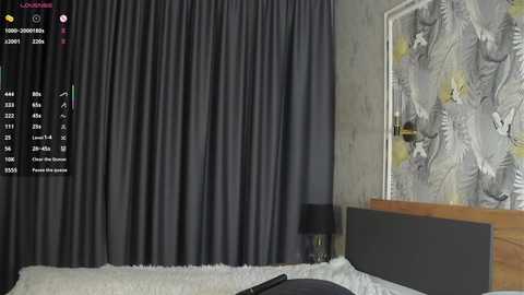 Video of a modern bedroom with a grey curtain, a wooden headboard, a lamp on a nightstand, and a floral-patterned wall.